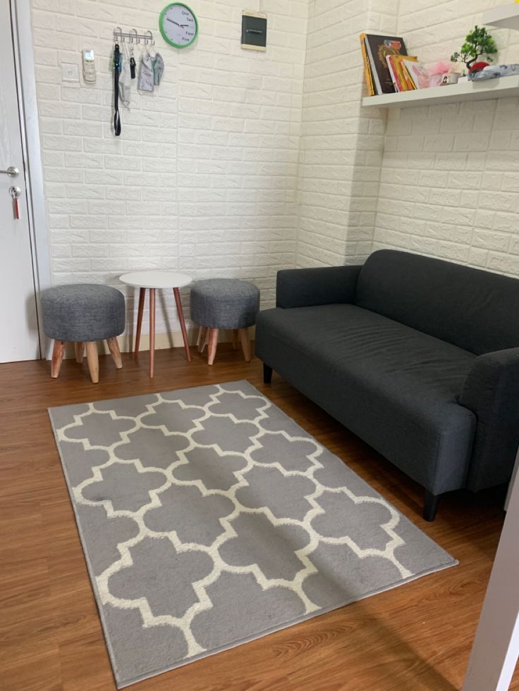 A gray patterned rug lies in front of a dark sofa, with exposed wood floor between them.