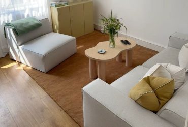 A tan rug beneath a pale sofa, an armless chair, and a curved wooden coffee table.