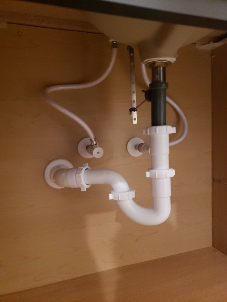 A white P-trap and flexible supply lines beneath a bathroom basin inside a wooden cabinet.