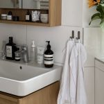 A white bathroom basin above a wooden vanity, with a mirrored cabinet, towels and sunflowers nearby.