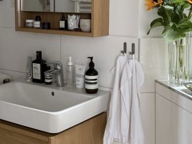 A white bathroom basin above a wooden vanity, with a mirrored cabinet, towels and sunflowers nearby.