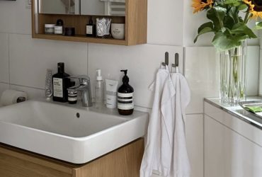A white bathroom basin above a wooden vanity, with a mirrored cabinet, towels and sunflowers nearby.