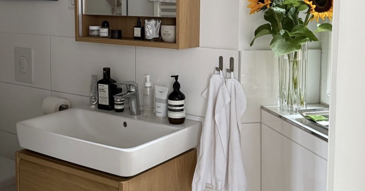 A white bathroom basin above a wooden vanity, with a mirrored cabinet, towels and sunflowers nearby.