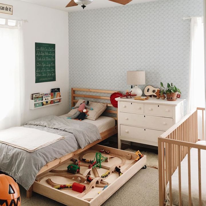 A shallow wooden tray of toy trains pulled out from beneath a bed.