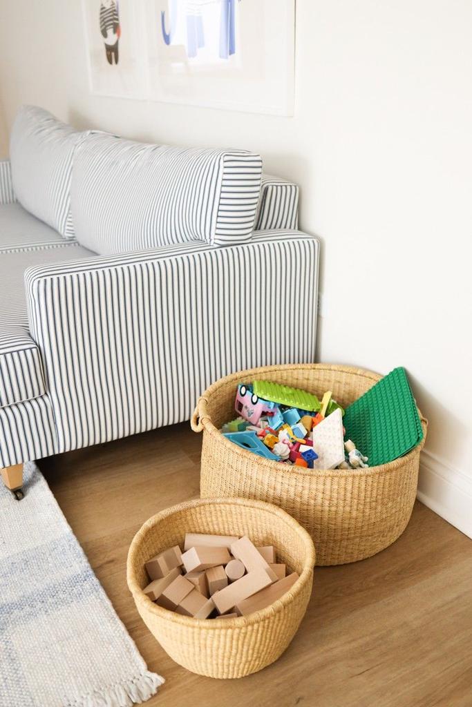 Two open woven baskets hold wooden blocks and colorful toys beside a striped sofa.